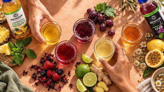 Degustação de cinco bebidas com frutas e ervas, vista de cima, com mãos escolhendo os copos.